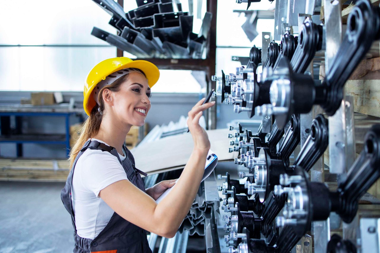 Woman industrial employee in working uniform and hardhat checking production in factory. Original equipment manufacturers